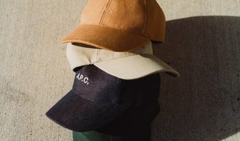 A.P.C. Men's Hats & Beanies - Stack of baseball caps on concrete.