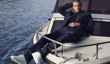 A.P.C. Men's Jeans - Man wearing patterned short sleeve shirt and blue jeans sitting in a backyard.