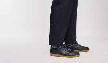 A.P.C. Men's Shoes - Man leaning on vintage car wearing grey coat and blue jeans.