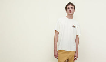 A.P.C. Men's T-shirts & Polos - Man in front of vintage car wearing brown raincoat and blue shirt.