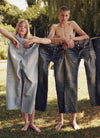 A woman and a man standing behind a clothesline with jeans hung