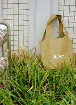 A.P.C. Ninon tote bag sitting in grass leaning on a wall