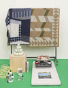 A.P.C. Lifestyle Gift Me More - Quilts, candles, books, and self care all displayed together in a room with a box and rolling rack.