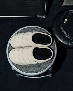 A.P.C. x Subu - Beige Subu sandals on round stool.