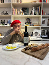 Jean Touitou sitting at a dining table with a wine bottle and a bread board