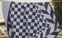 Blue and white patchwork quilt n a rope line near a lake.
