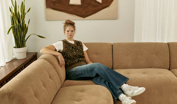 A.P.C. Women's Shoes - Woman wearing knit vest and blue jeans sitting on large couch.