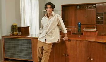 A.P.C. Men's Suits & Blazers - Man leaning on kitchen counter wearing white corduroy shirt and brown pants.