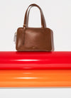 A brown leather A.P.C. bag on top of colorful surface