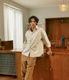 Male model wearing a ecru shirt and brown pants in a livingroom
