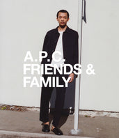 A.P.C. Men All - Man wearing blue jacket and pants leaning against pole.